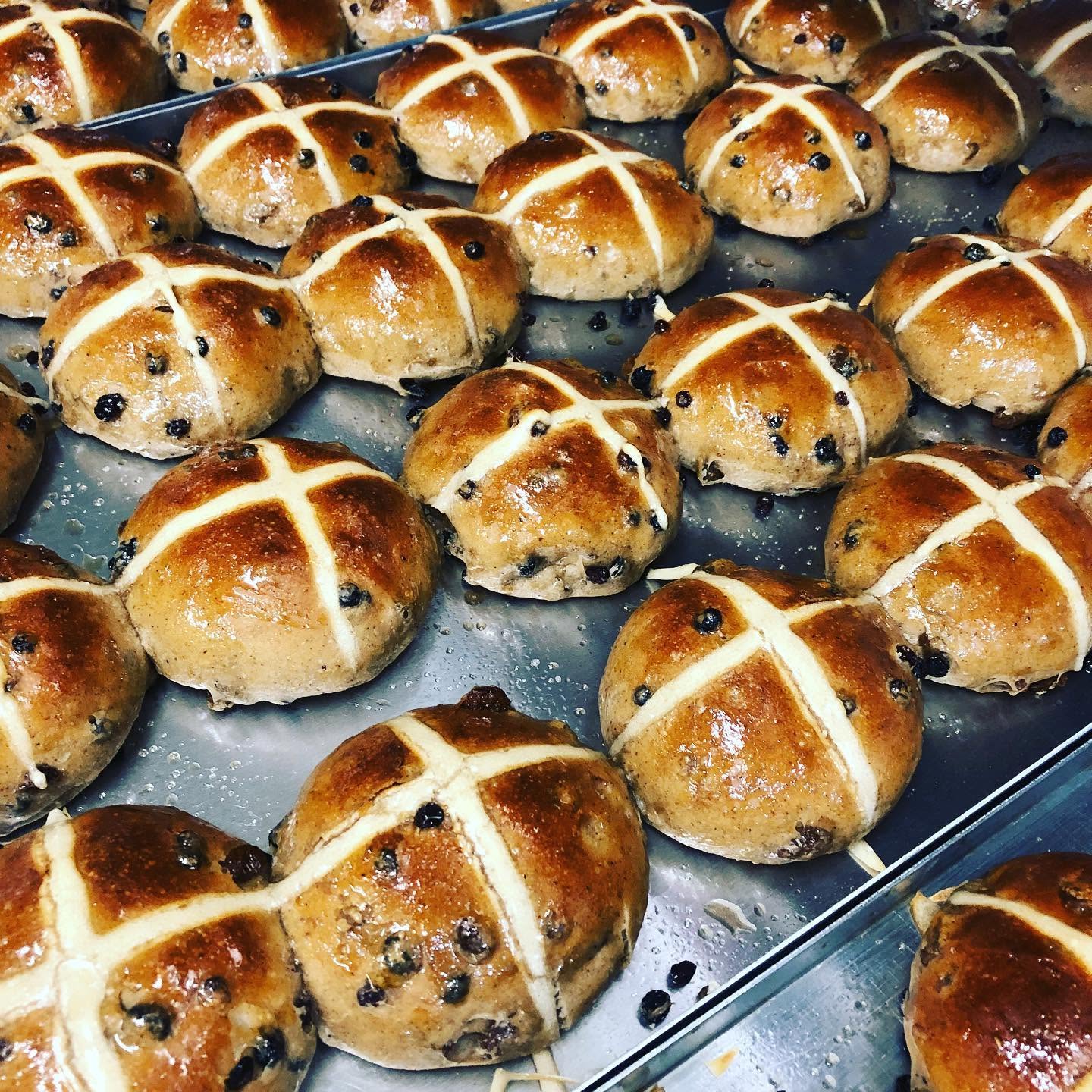 Baked hot cross buns on a tray with a cross-shaped topping.